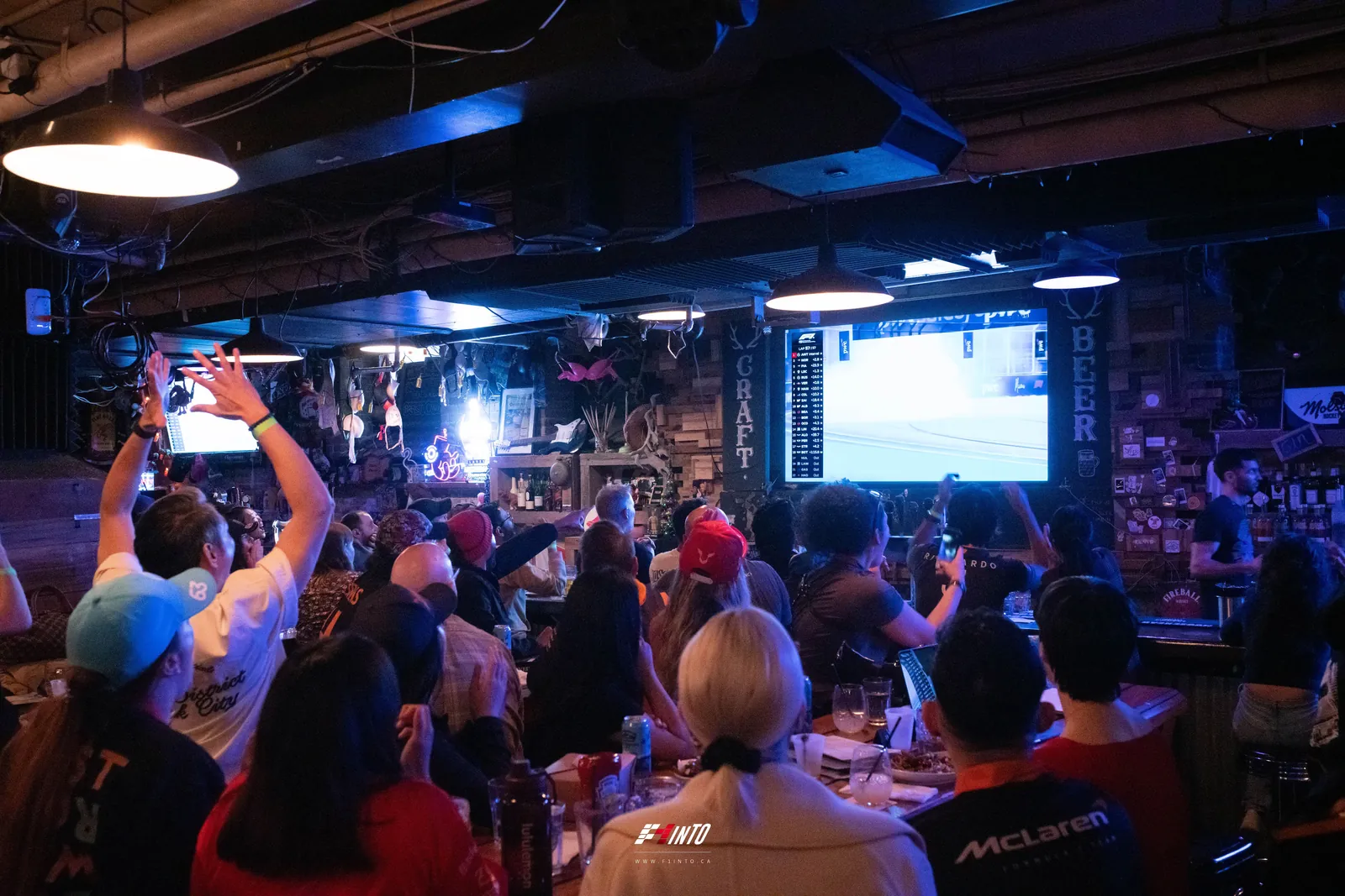 An F1inTO race day room on its feet, arms up at the big screen during the Miami Grand Prix