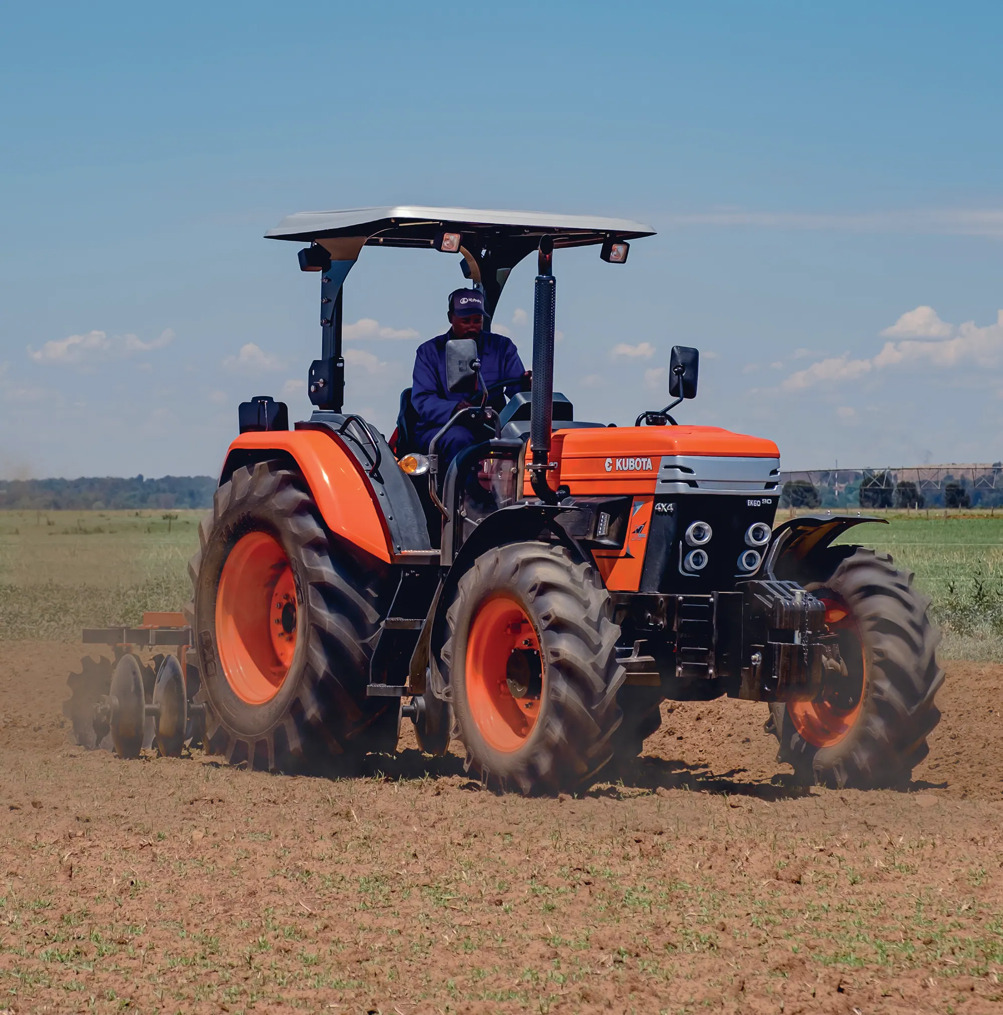Farmer driving an orange E-Kubota tractor with a canopy across a dry field