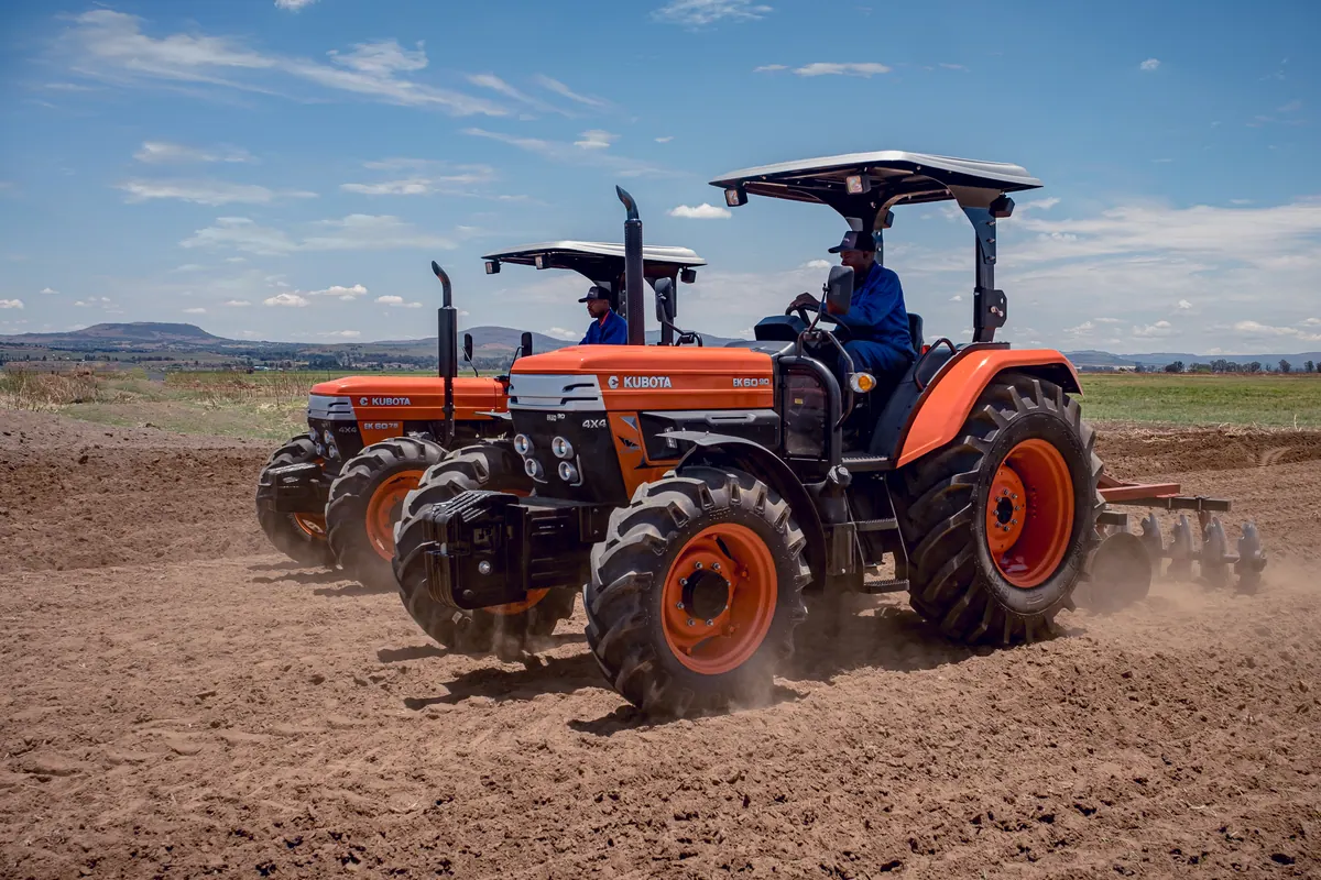Two orange E-Kubota tractors working a freshly tilled field