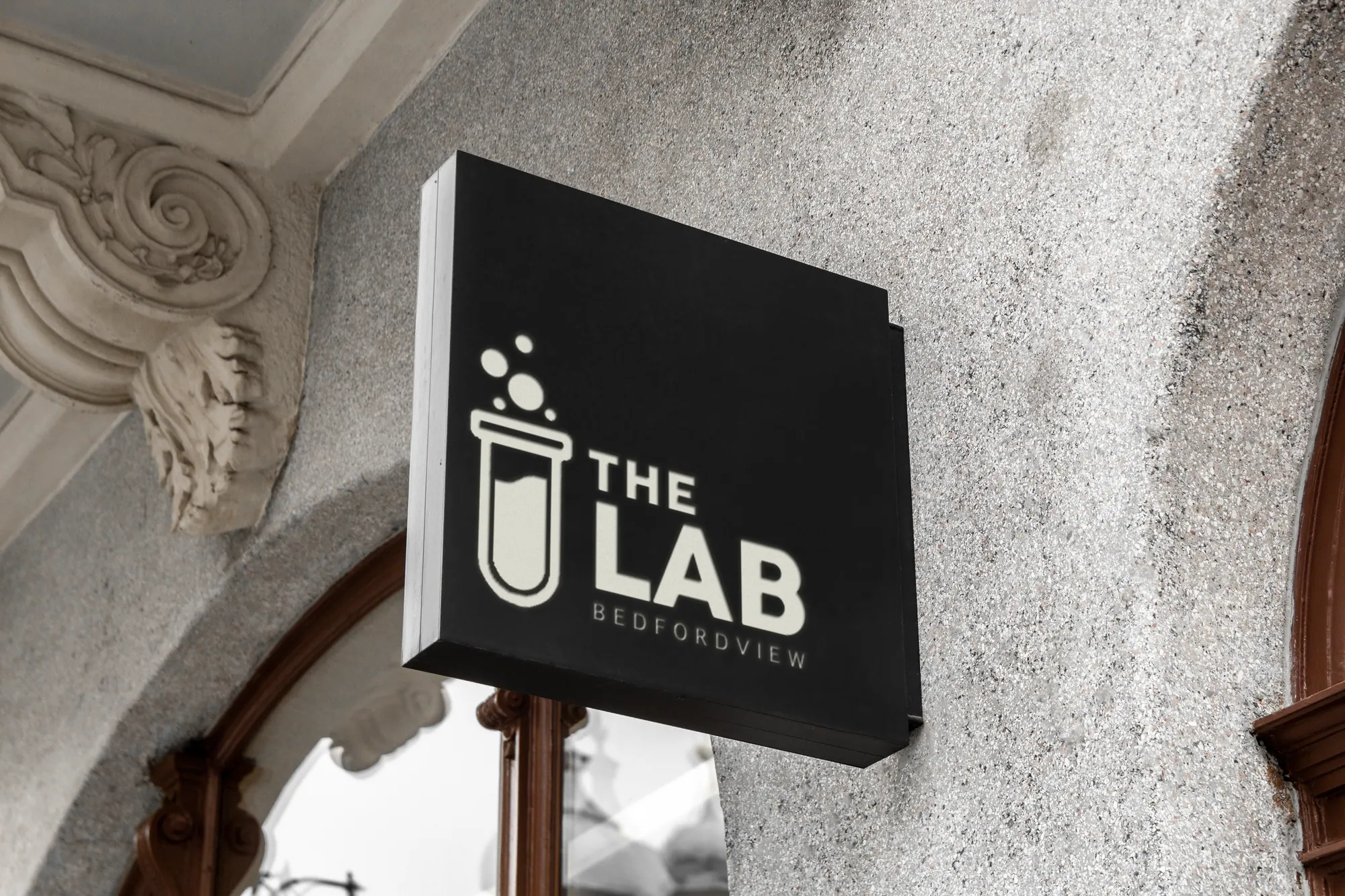 Black hanging sign with The Lab test tube logo on a stone facade
