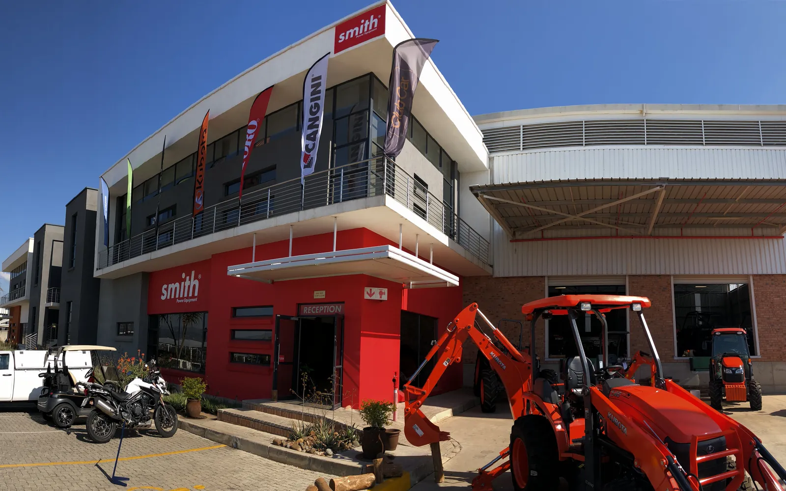 The Smith Power Equipment head office and warehouse under brand flags for Kubota, Toro, Cangini and Club Car, two Kubota tractors out front